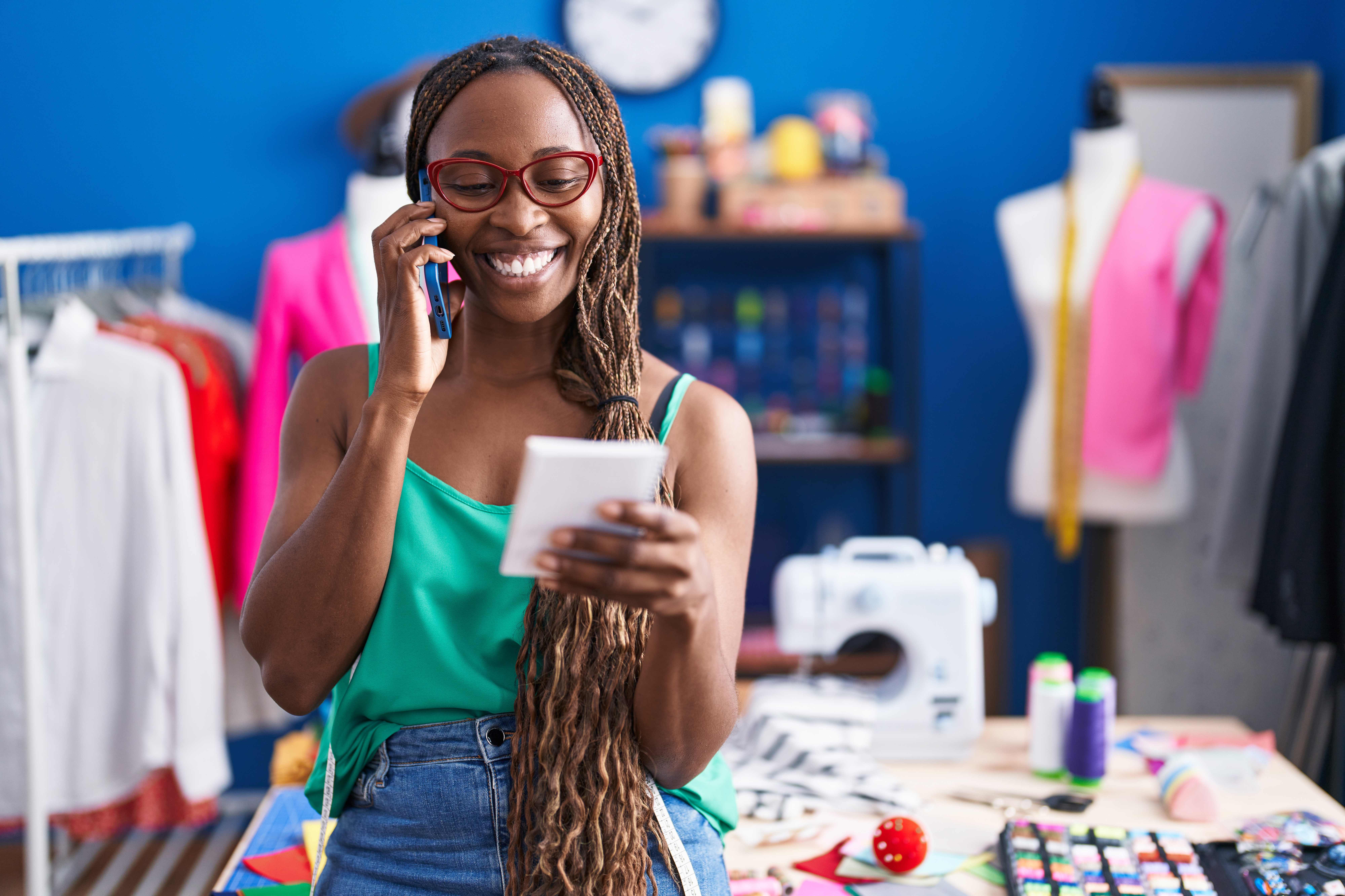 African woman business owner talking on smartphone while reviewing business documents in her workspace